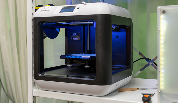En 3D-skrivare ses från sidan, med några verktyg liggande bredvid