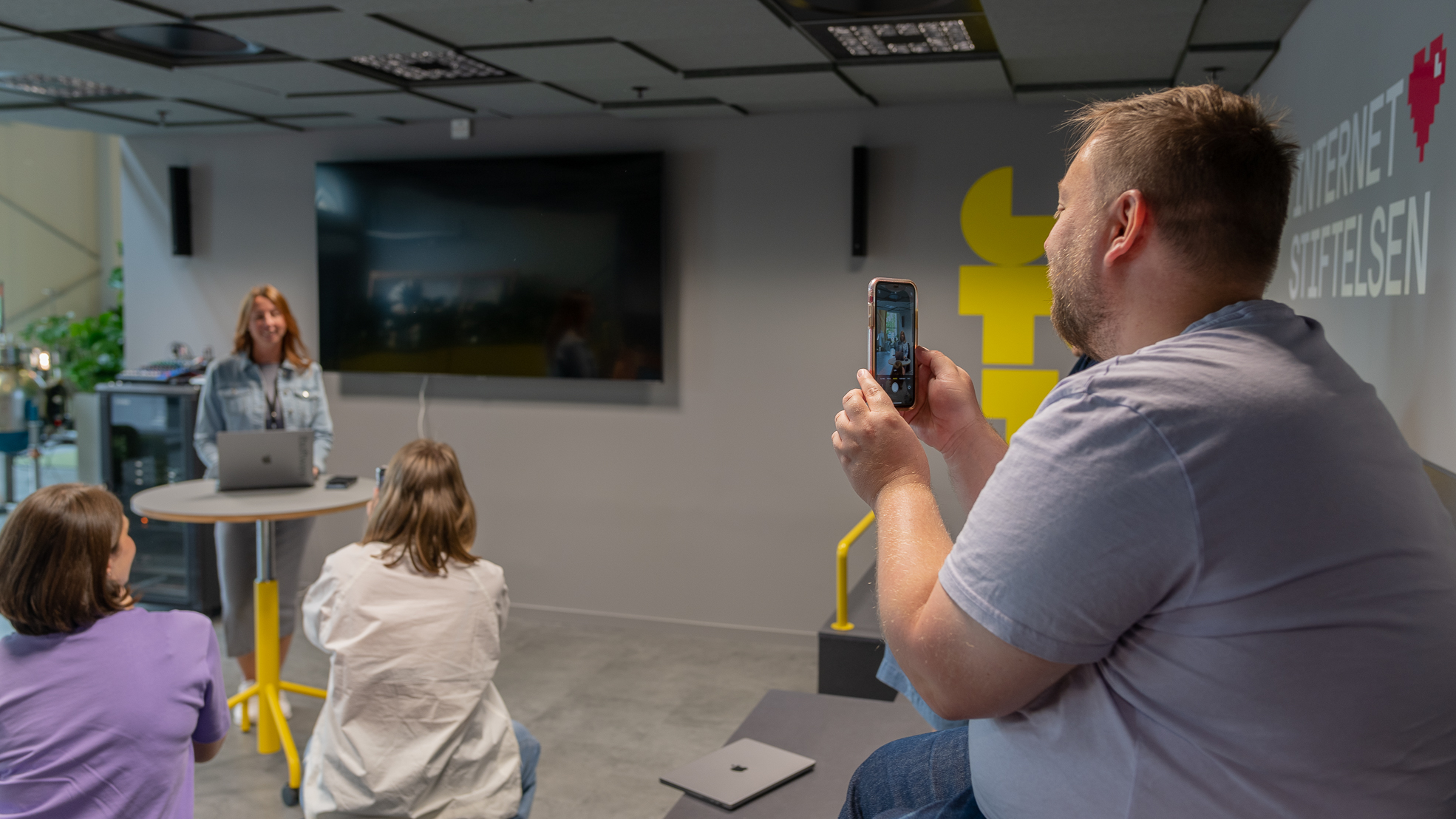 En man i publiken fotograferar en talare med sin mobil i eventytan på Goto 10. Vi ser honom bakifrån