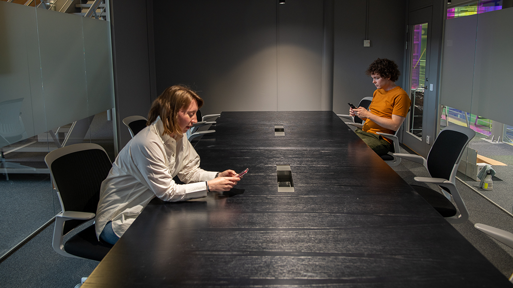 Två personer sitter vid ett långt, svart bord i ett mötesrum.