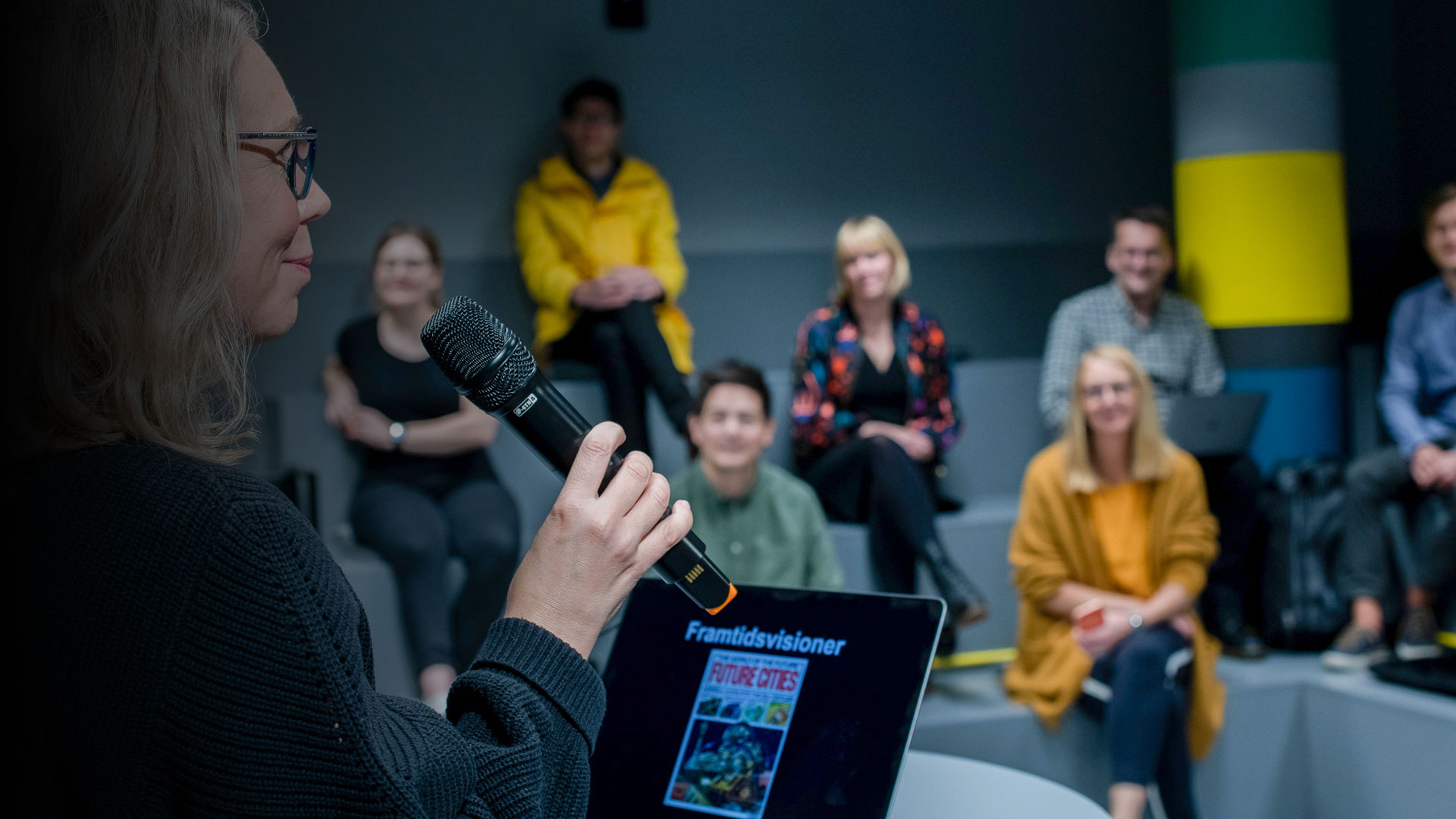 En kvinna pratar i mikrofon framför publik.